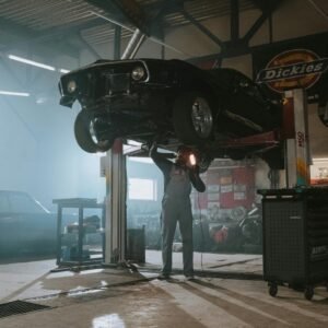 Male mechanic using a light to inspect a classic car lifted in an automotive garage.