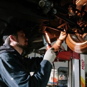 Mechanic examining car's undercarriage at a garage, focusing on vehicle maintenance.
